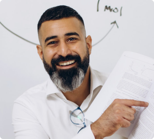 Head Of Chemistry Davinder Bhachu, experienced educator, in front of a whiteboard holding an opened book